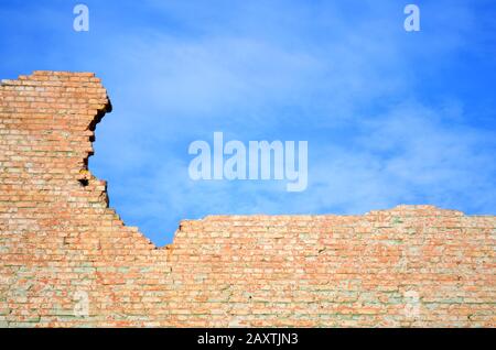 Muro di mattoni rossi in frantumi contro il cielo blu Foto Stock