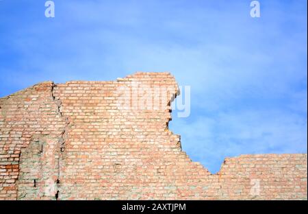 Muro di mattoni rossi in frantumi contro il cielo blu Foto Stock