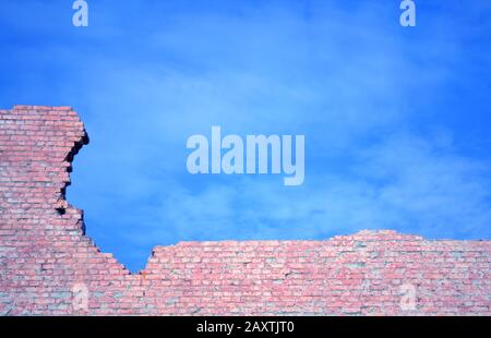 Muro di mattoni rossi in frantumi contro il cielo blu Foto Stock