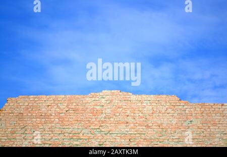 Muro di mattoni rossi in frantumi contro il cielo blu Foto Stock