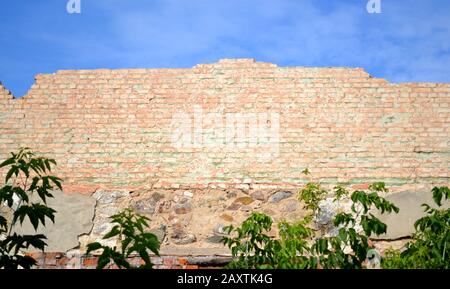 Muro di mattoni rossi in frantumi contro il cielo blu Foto Stock