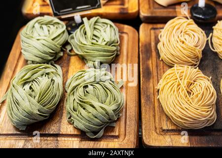 Tagliatelle verdi con spinaci e verdure arrosto crostate da vicino su vassoi di legno nel negozio. Pasta italiana cruda. Cucina vegetariana. Foto Stock