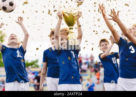 Squadra di calcio giovanile campione con trofeo vincente. La squadra di calcio maschile celebra la vittoria nella competizione scolastica alzando la coppa d'oro. Anche i bambini sono felici Foto Stock