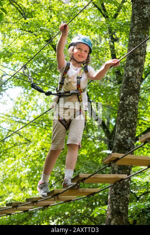 Ragazza giovane ragazza bambino bambino su un bambino ostacolo corso attività Trail in alto nel bosco foresta albero, in un parco avventura in Francia durante l'estate. (112) Foto Stock