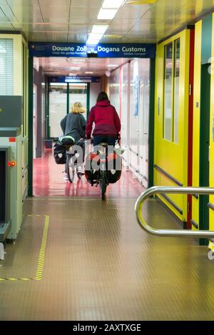 Due ciclisti turisti in bicicletta / passare attraverso Dogana / Douanes al confine tra la Francia e la Svizzera alla stazione ferroviaria di Ginevra. (112) Foto Stock