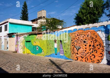 Strada laterale a Oaxaca, Messico, con pareti di arte di strada che raffigurano animali e popolazioni indigene Foto Stock