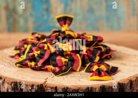 Pasta farfalle italiana cruda multicolore a spicchio su tavola rustica Foto Stock