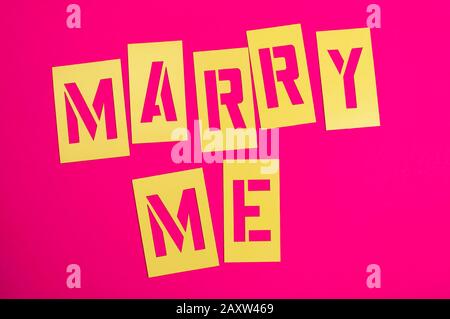 Marry Me messaggio scritto in caratteri stencil gialli su sfondo rosa brillante Foto Stock