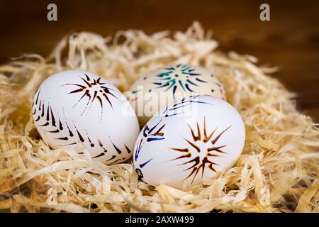 Tre uova di Pasqua decorate nel nido di trucioli di legno su sfondo sfocato. Conchiglie vuote a motivi casuali dipinte con tecnica di cera nella vita artistica. Foto Stock