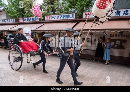 Giappone, Tokyo: Coppia sposata in costume tradizionale, in risciò ad Asakusa, risciò tirato da un uomo, con due uomini davanti che tengono lanterne Foto Stock