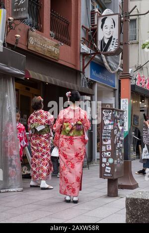 Giappone, Tokyo: Due donne in kimono visto da dietro di fronte a un kimono e negozio di abbigliamento tradizionale giapponese nel quartiere di Asakusa Foto Stock