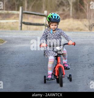 determinata bambina imparare a guidare la bicicletta con ruote di allenamento in paese Foto Stock