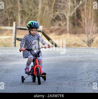 determinata bambina imparare a guidare la bicicletta con ruote di allenamento in paese Foto Stock