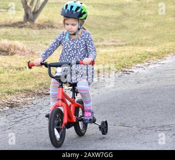 determinata bambina imparare a guidare la bicicletta con ruote di allenamento in paese Foto Stock