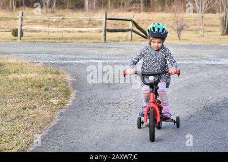 determinata bambina imparare a guidare la bicicletta con ruote di allenamento in paese Foto Stock