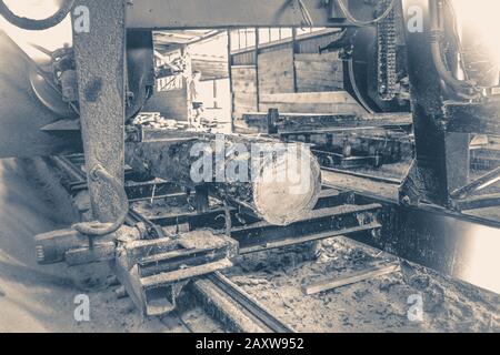 Foto in vecchio stile vintage. Segheria. Processo di lavorazione dei tronchi in attrezzatura sega sega a macchina sega a macchina il tronco di albero sulle tavole di asse. Foto Stock