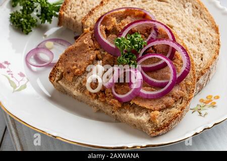 Strutto di maiale mescolato con crepitings macinati su una fetta di pane, con anelli di cipolla e prezzemolo Foto Stock