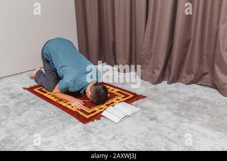 Un giovane prega e recita il Corano musulmano su un piccolo tappeto portatile all'interno. Religione e concetto rituale Foto Stock