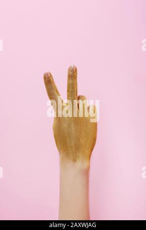 Mano donna con glitter dorato che mostra il gesto della vittoria su sfondo rosa. Foto Stock