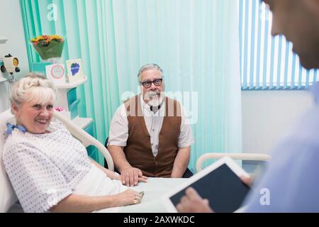 Dottore con tablet digitali che fa giri, parlando con le coppie senior in stanza ospedale Foto Stock