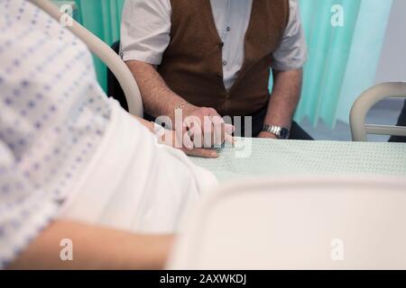 Affettuoso anziano che tiene le mani con la moglie che riposa nel letto dell'ospedale Foto Stock