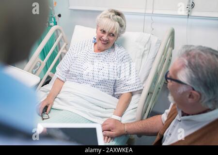 Affettuoso anziano che parla con la moglie che riposa nel letto dell'ospedale Foto Stock