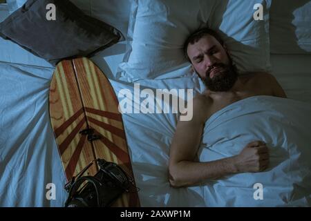 Un uomo dorme nel sangue con il suo amato snowboard. Il ragazzo pupazzo di snowboarder che dorme bene Foto Stock