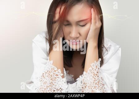 Donna asiatica in merletto da notte e bianchi accappatoi in raso ha un mal di testa, isolato su sfondo grigio. Emicrania sofferente. Foto Stock