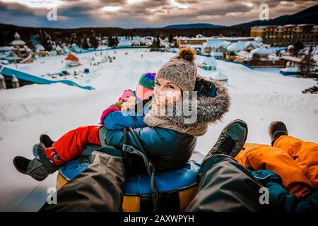 Madre scivola con la sua famiglia sui tubi durante una giornata invernale Foto Stock