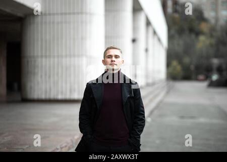 Uomo serio in trenchcoat nero e collo polo viola Foto Stock