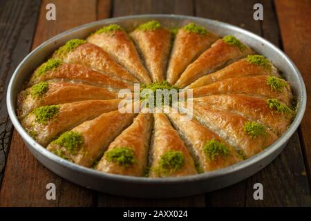Closeup di baklava tagliato a fette in una padella con crema di pistacchio crudo su un tavolo di legno Foto Stock