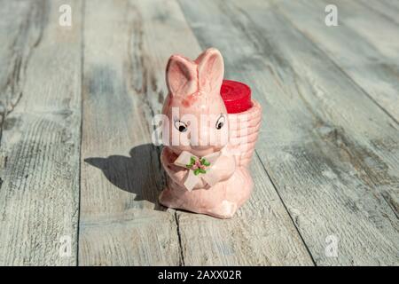 Coniglietto di coniglio di Pasqua. Focus selettivo su decorativo ceramica rosa coniglietto di pasqua su rustico tavolo di legno grigio. Decorazioni pasquali sfondo. All'Aperto. Foto Stock