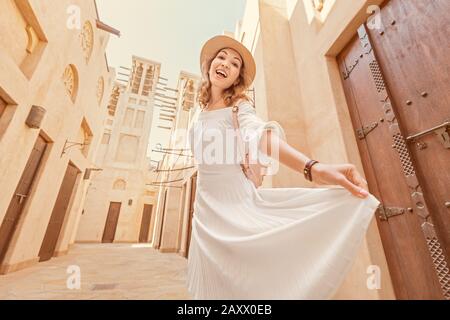 Ragazza asiatica felice in abito bianco a piedi tra le strette strade della città vecchia da qualche parte in Medio Oriente. Destinazioni di viaggio e concetto di turismo Foto Stock