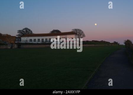 La luna quasi piena super 'adesso' che sorge sopra il lago di nautica edificio sul lungomare della scogliera ovest di Ramsgate Foto Stock