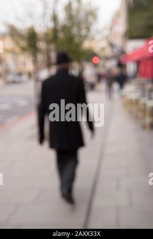 Vista posteriore della misteriosa figura sfocata in cappello nero e cappotto, strada di Londra a piedi sul marciapiede. Strano mistero uomo, agente segreto, spia sotto copertura. Foto Stock