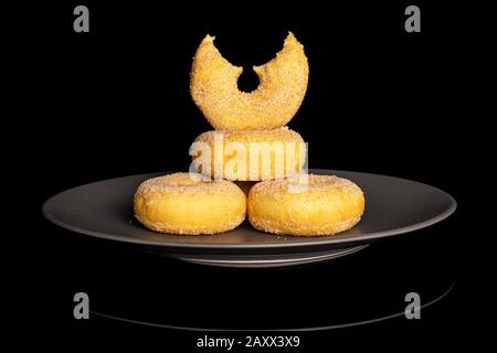 Gruppo di quattro interi una metà di ciambella di mini cannella dorata dolce su piastra di ceramica grigia isolata su vetro nero Foto Stock