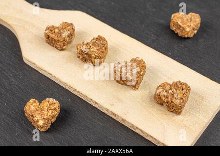 Gruppo di sei cuore di cereali marrone intero sano con cacao su una piccola tavola da taglio in legno su pietra grigia Foto Stock