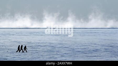 Silhouette di tre persone che camminano su un grande fiume ghiacciato in una fredda giornata di sole Foto Stock