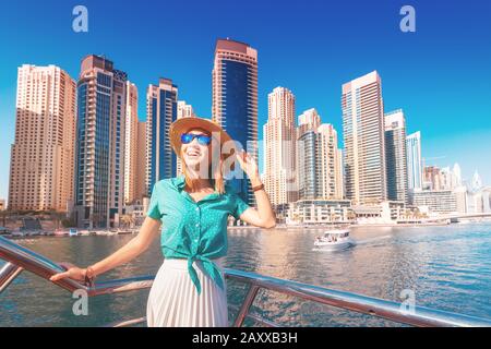 Allegro viaggiatore ragazza su una barca traghetto che naviga attraverso il porto di Dubai Marina tra enormi grattacieli. Concetto di turismo negli Emirati Arabi Uniti Foto Stock