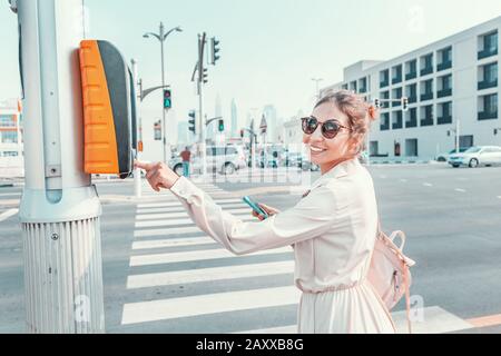 Ragazza pedonale preme il pulsante per attraversare la strada in modo sicuro. Design urbano di una città sicura Foto Stock