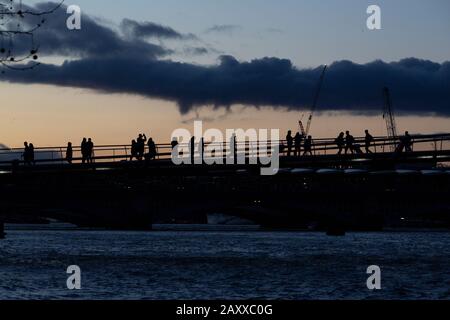 Londra, Regno Unito. 13th Feb, 2020. Il tramonto, un pendolari che attraversa il Millennium Bridge, si ferma per scattare una foto guardando verso ovest lungo il Tamigi durante l'alta marea primaverile. Credito: Thamesfleet/Alamy Live News Foto Stock