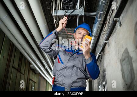 Lavoratore Maschile Che Indossa Hard Hat Con Un Multimetro Foto Stock