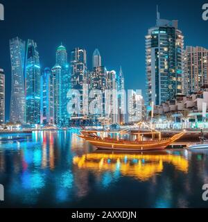Luci multicolore della città notturna nel quartiere di Dubai Marina. Antica nave araba stilizzata Abra Dhow con luci in primo piano.