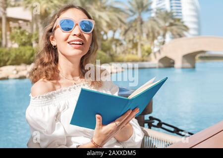 Sorridente ragazza legge menu al bar o ristorante sulla terrazza mentre si rilassa presso il resort sul mare Foto Stock