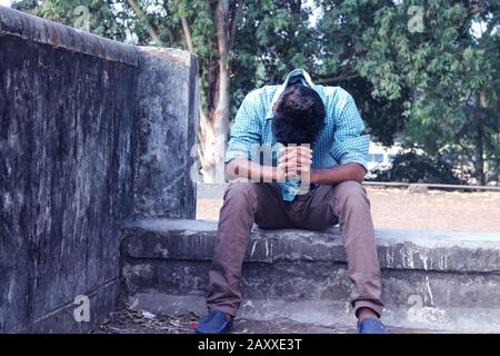 Depresso Teenager uomo seduto da solo a parete in Outdoor.Sgradevoli dolore. Triste triste bell'uomo.Bangladeshi e ragazzo asiatico Che Soffrono depressione. Foto Stock