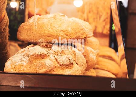 Pane fresco di grandi crostacy rotondo loafs con farina accatastata sopra l'un l'altro in un panificio / negozio di stallo del mercato i dintorni. Colori caldi, luce Foto Stock