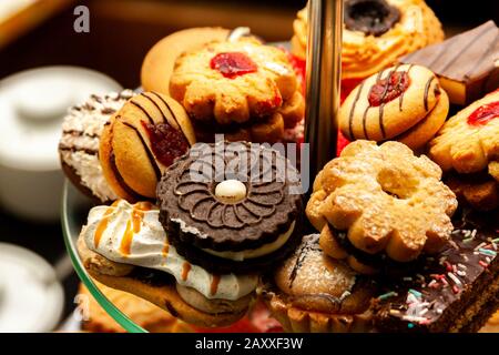 Gruppo di molti piccoli gustosi piccoli spuntini dolci, piccole torte. Un sacco di mini cupcakes zuccherati accatastati palancole su un piatto livellato fotografia macro Foto Stock