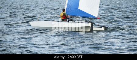 Bambini che navigano in una piccola e colorata barca a catamarano con una vela blu e bianca su una via navigabile interna. Junior Sailor in gara su acqua salata Lago Mac Foto Stock