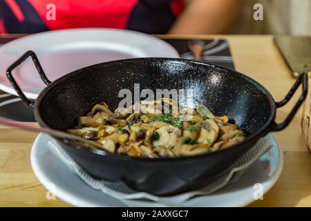 Sul tavolo da pranzo si trova una padella calda con champignons in salsa all'aglio. Vista orizzontale, closeup. Messa a fuoco centrale selettiva e riduzione sfocata. Foto Stock