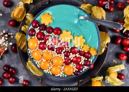 Ciotola di frullato di frutta con polvere di spirulina verde naturale sana decorata con mirtilli rossi, phisalis e frutti kaki e quinoa purè Foto Stock